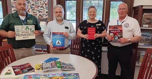 Four people holding up books behind round table in library