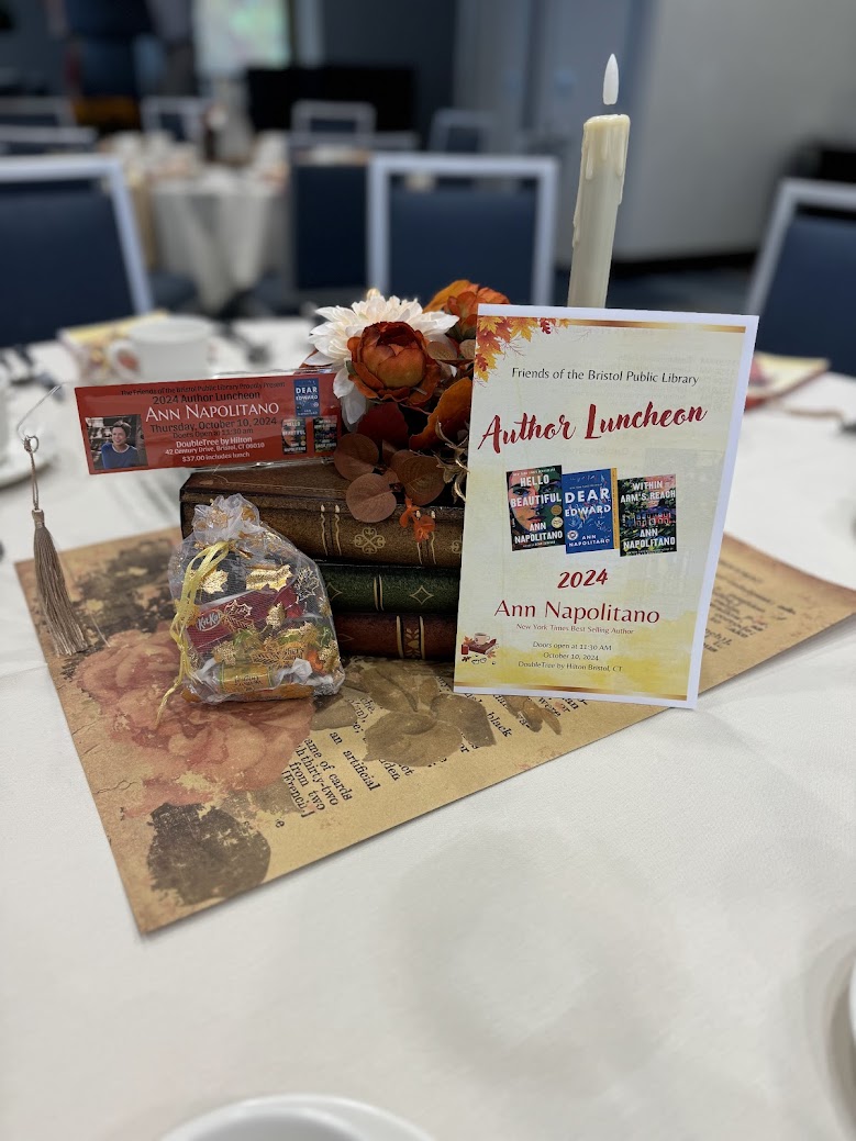 centerpiece on table with flowers, candle, sachet of candy, and event program for 2024 Author Luncheon.