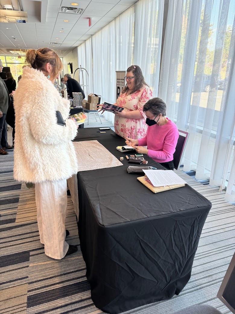 Author Ann Napolitano sitting at table signing book for woman standing across the table.